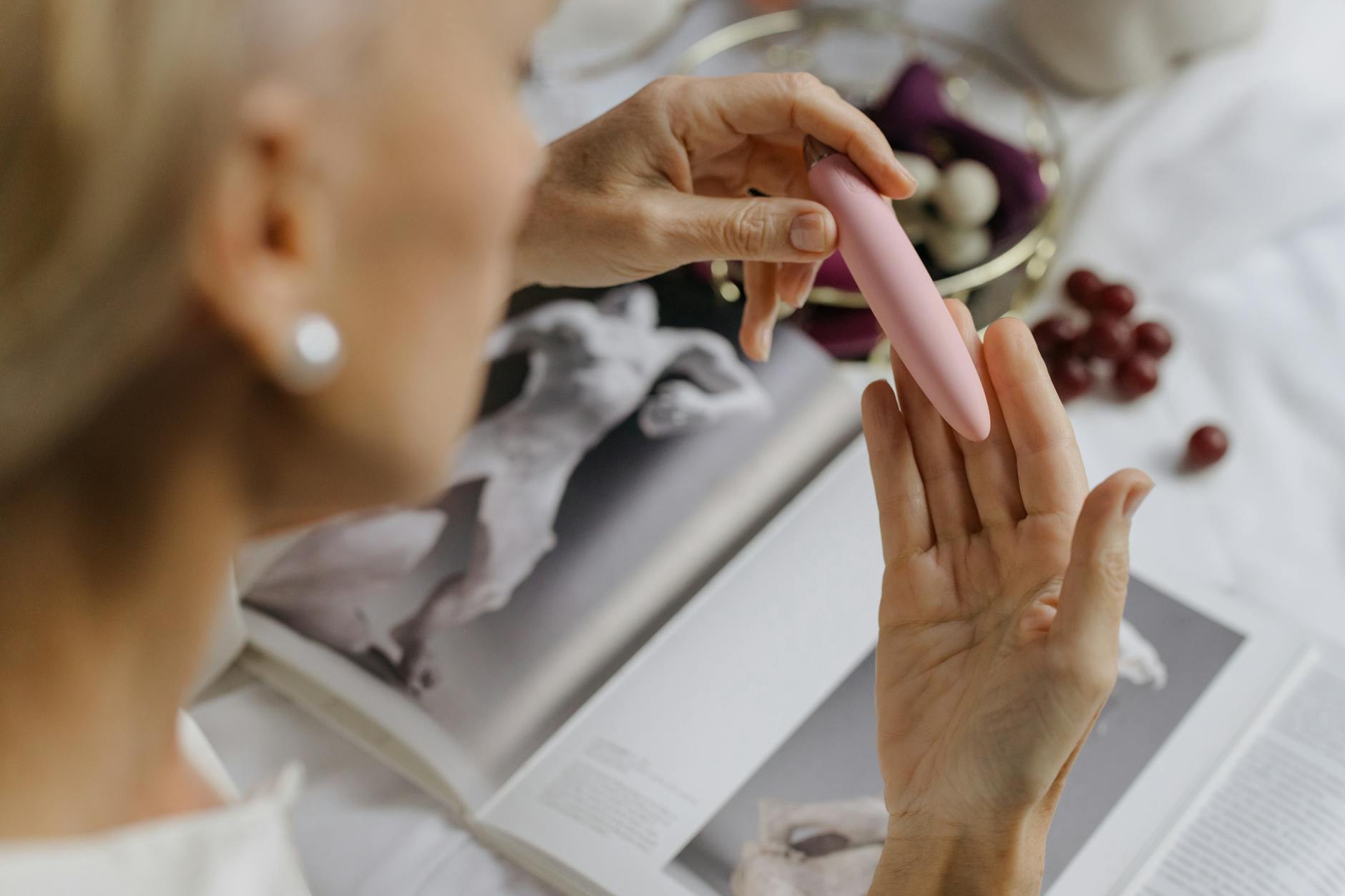 Close-up of a woman holding a pink vibrator with art books in background, emphasizing intimate personal wellness