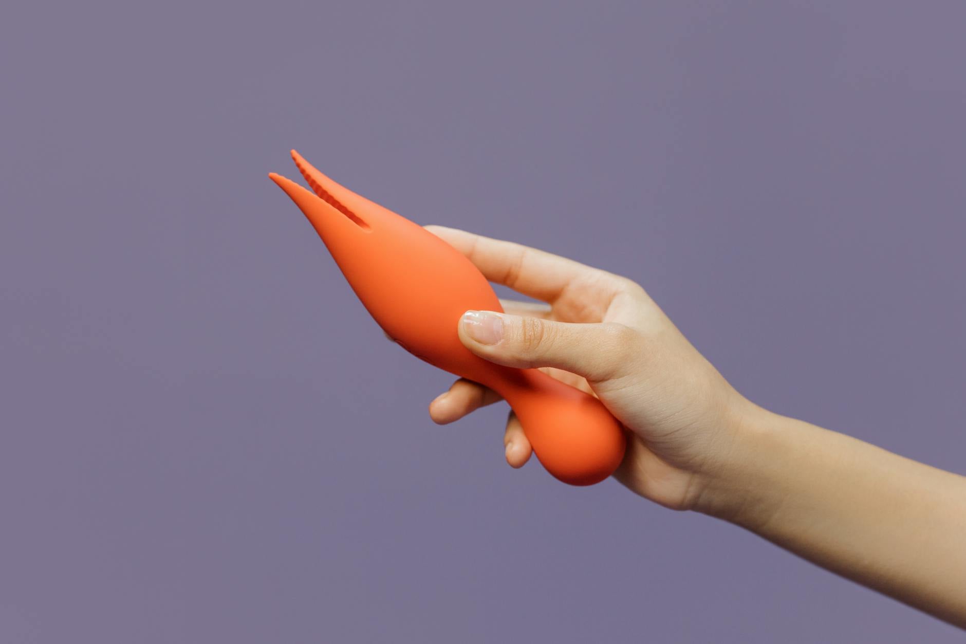 A close-up of a hand holding an orange lemon vibrator against a minimalistic purple backdrop, showcasing modern sensuality.