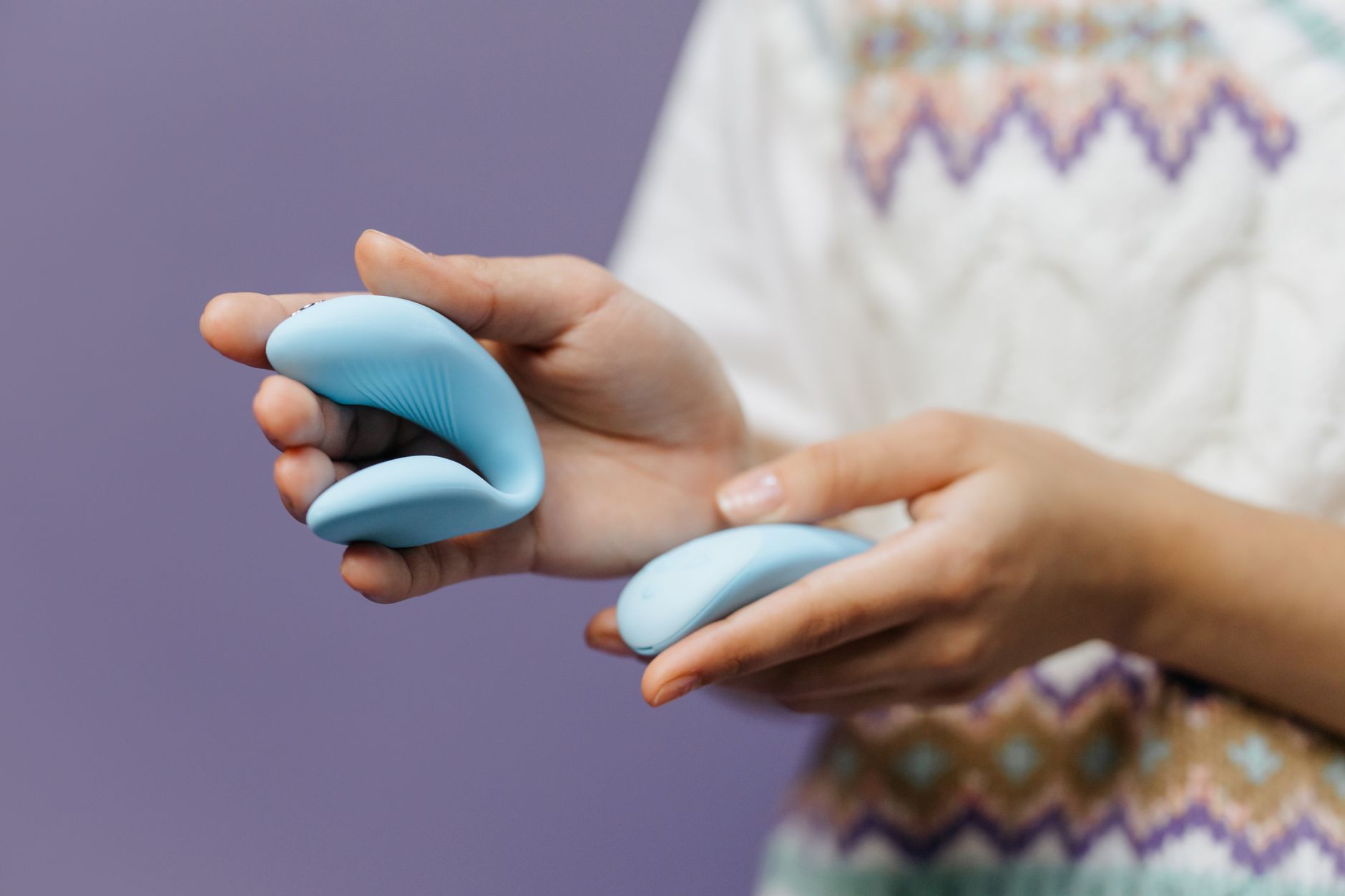 Close-up of hands holding a sleek lemon vibrator against a soft purple background