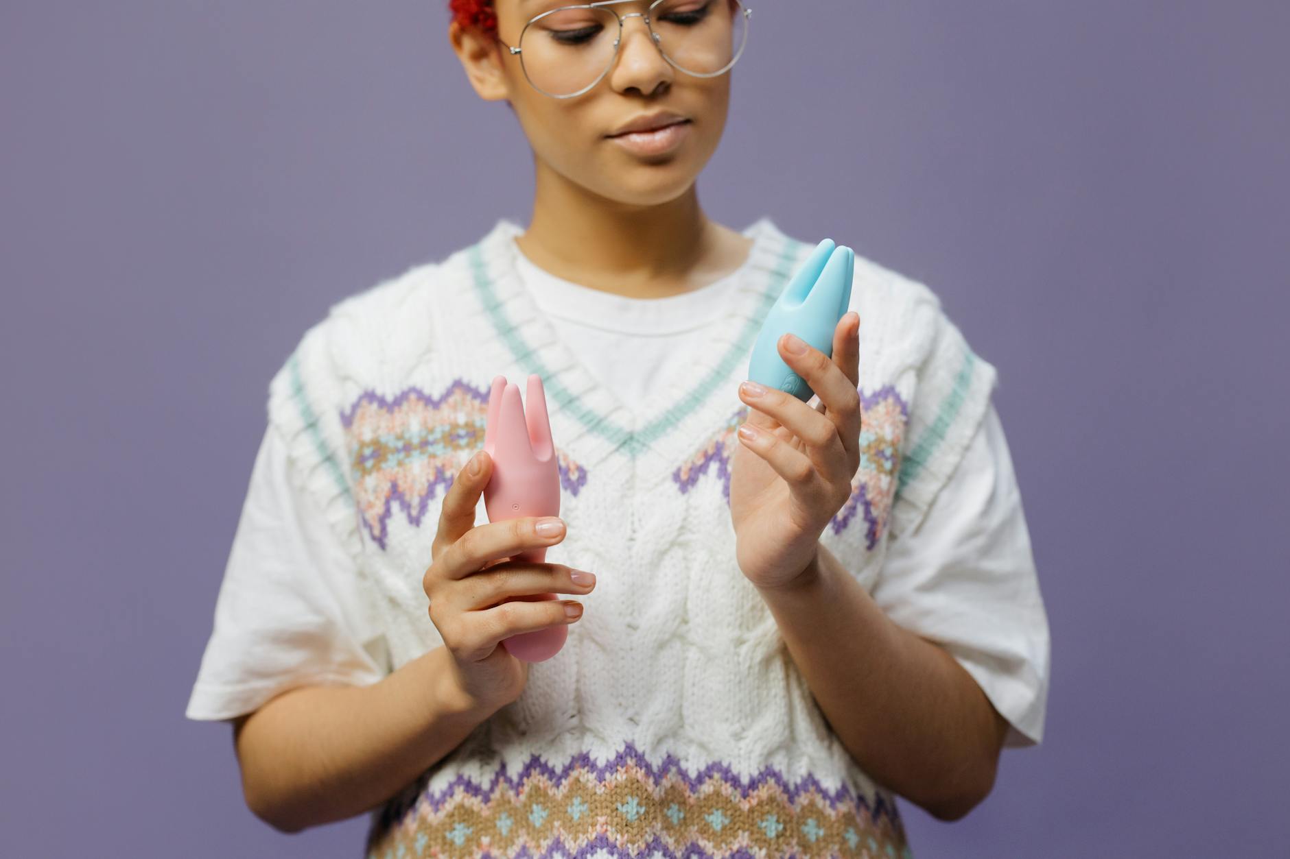 Woman holding blue and pink silicone vibrators in a contemplative manner, exploring pleasure privately